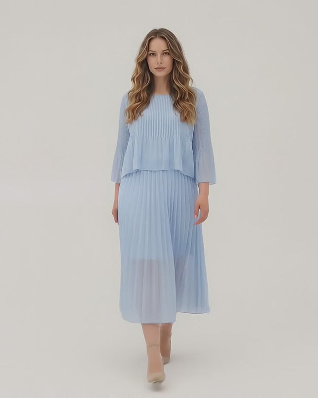 Ένα plus size μοντέλο περπατάει αργά προς την κάμερα σε περιβάλλον στούντιο με ουδέτερο φόντο φορώντας το Επίσημο μάξι πλισέ φόρεμα σε γαλάζιο χρώμα