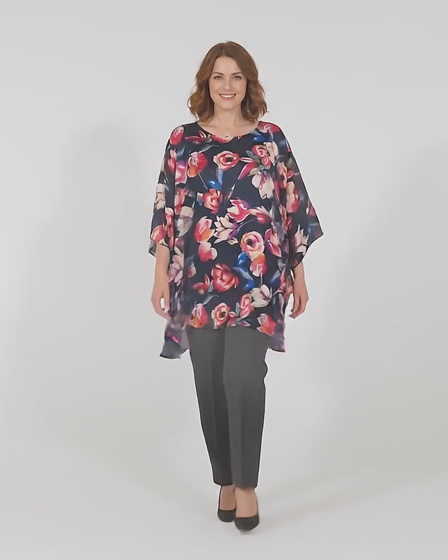 Βίντεο παρουσίασης σε στούντιο με ουδέτερο φόντο όπου ένα plus size μοντέλο περπατάει αργά προς την κάμερα φορώντας Επίσημη σκούρο μπλε φλοράλ μάξι τουνίκ πόντσο μεγάλα μεγέθη