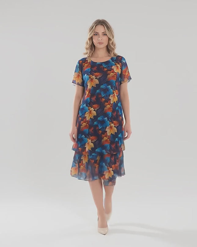 Ένα γυναικείο μοντέλο περπατάει αργά προς την κάμερα σε περιβάλλον στούντιο με ουδέτερο φόντο φορώντας το Επίσημο σκούρο μπλε μάξι φόρεμα από σιφόν plus size με μοτίβο φύλλων