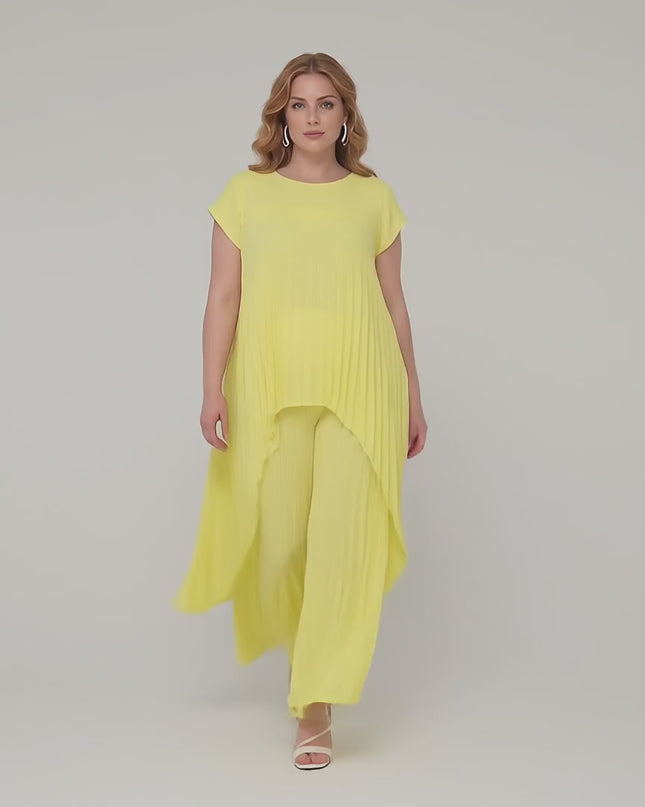 Ένα plus size μοντέλο περπατάει αργά προς την κάμερα σε περιβάλλον στούντιο με ουδέτερο φόντο φορώντας το Κίτρινο επίσημο σετ με ασύμμετρη τουνίκ και παντελόνα plus size
