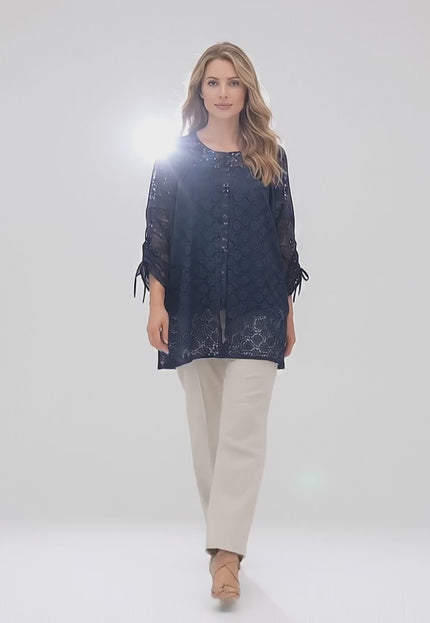 Βίντεο παρουσίασης όπου ένα plus-size μοντέλο περπατάει αργά προς την κάμερα σε περιβάλλον στούντιο με ουδέτερο φόντο φορώντας το προϊόν Επίσημη γυναικεία τουνίκ με φλοράλ δαντέλα σε σκούρο μπλε