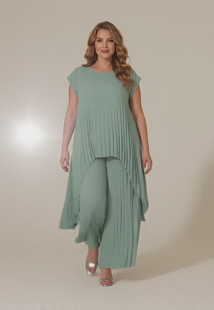 Ένα plus-size γυναικείο μοντέλο περπατάει αργά προς την κάμερα σε ένα στούντιο με ουδέτερο φόντο φορώντας το προϊόν Αμπιγιέ Σετ Τουνίκ Και Παντελόνα Ανοιχτό Πράσινο Μεγάλα Μεγέθη