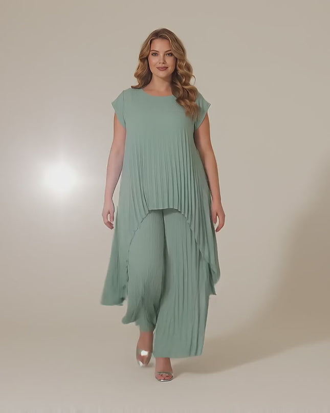 Ένα plus-size γυναικείο μοντέλο περπατάει αργά προς την κάμερα σε ένα στούντιο με ουδέτερο φόντο φορώντας το προϊόν Αμπιγιέ Σετ Τουνίκ Και Παντελόνα Ανοιχτό Πράσινο Μεγάλα Μεγέθη