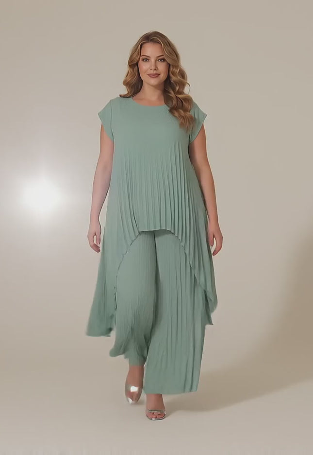 Ένα plus-size γυναικείο μοντέλο περπατάει αργά προς την κάμερα σε ένα στούντιο με ουδέτερο φόντο φορώντας το προϊόν Αμπιγιέ Σετ Τουνίκ Και Παντελόνα Ανοιχτό Πράσινο Μεγάλα Μεγέθη