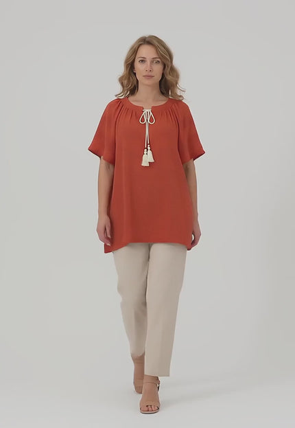Ένα plus size μοντέλο περπατάει αργά προς την κάμερα σε περιβάλλον στούντιο με ουδέτερο φόντο φορώντας το προϊόν Επίσημη μάξι τουνίκ με boho λεπτομέρειες κεραμιδί