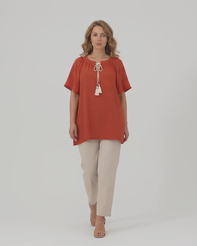 Ένα plus size μοντέλο περπατάει αργά προς την κάμερα σε περιβάλλον στούντιο με ουδέτερο φόντο φορώντας το προϊόν Επίσημη μάξι τουνίκ με boho λεπτομέρειες κεραμιδί