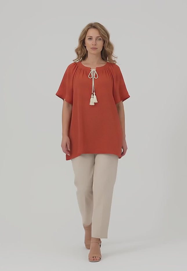 Ένα plus size μοντέλο περπατάει αργά προς την κάμερα σε περιβάλλον στούντιο με ουδέτερο φόντο φορώντας το προϊόν Επίσημη μάξι τουνίκ με boho λεπτομέρειες κεραμιδί
