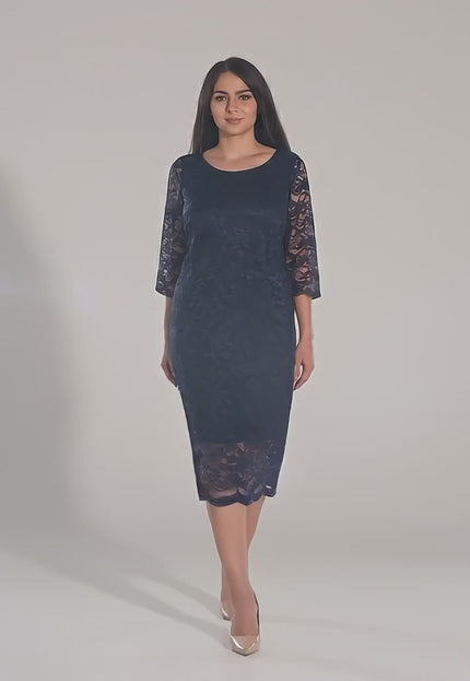 Ένα plus-size μοντέλο περπατάει αργά προς την κάμερα σε περιβάλλον στούντιο με ουδέτερο φόντο παρουσιάζοντας και φορώντας το προϊόν Σκούρο Μπλε Φόρεμα- Στρογγυλή Λαιμόκοψη - Κάτω από το Γόνατο - Άνοιξη-Καλοκαίρι