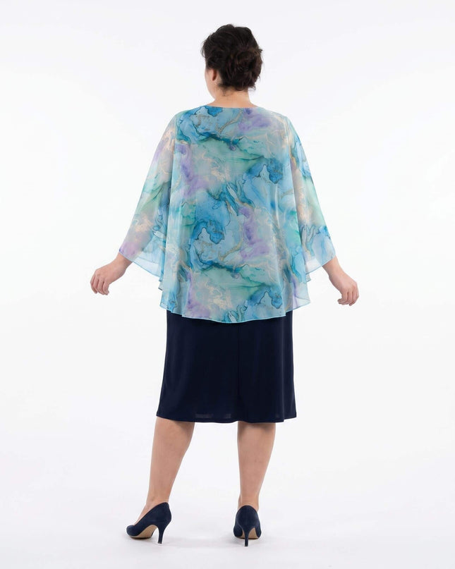 Ολόσωμη λήψη από την πίσω όψη του σκούρου μπλε επίσημου φορέματος σε μεγάλα μεγέθη, που αναδεικνύει την αέρινη κάπα από σιφόν με ακουαρέλ print.