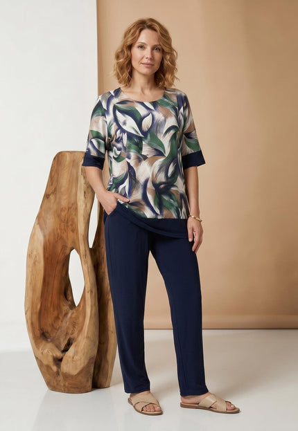 Ολόσωμη λήψη σε γυναικείο plus size σετ, το οποίο περιλαμβάνει σκούρο μπλε παντελόνι σε ίσια γραμμή και κοντομάνικη τουνίκ με print φύλλων.