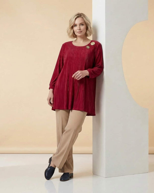 Γυναίκα φοράει κόκκινη τουνίκα και μπεζ παντελόνι και στέκεται σε στούντιο δίπλα σε διακοσμητική κατασκευή