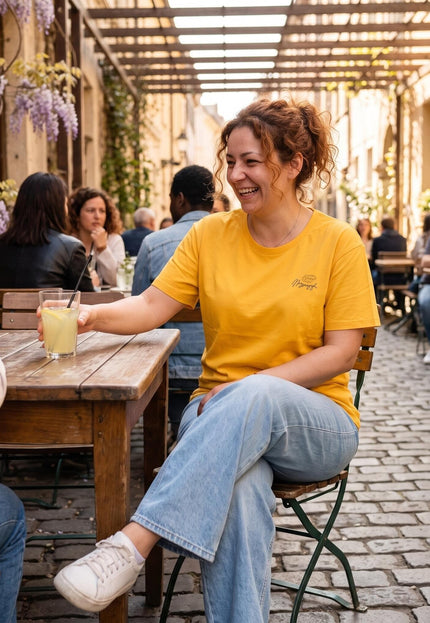 Γυναικείο κίτρινο t-shirt plus size με διακριτικό σχέδιο στο στήθος, φορεμένο από χαμογελαστή γυναίκα σε εξωτερικό χώρο καφετέριας.
