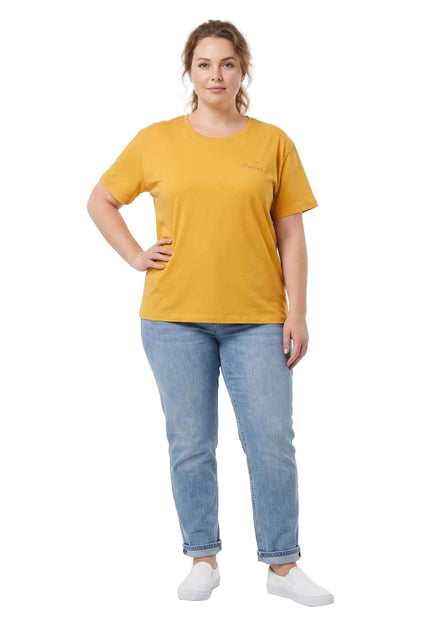 Ολόσωμη λήψη σε λευκό φόντο με γυναικείο t-shirt plus size σε μουσταρδί χρώμα, συνδυασμένο με τζιν παντελόνι.